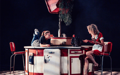 Sur une scène de théâtre, deux femmes autour d'une table de dinner