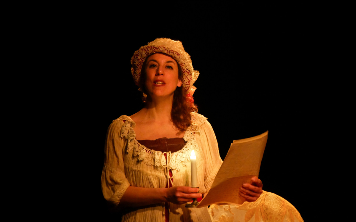 Sur fond noir, une femme lit un papier, éclairé à la bougie