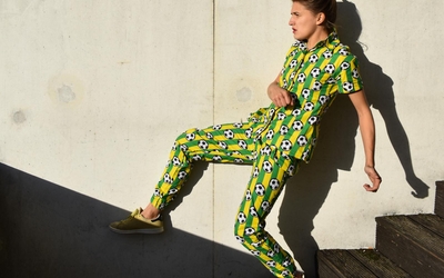 Une femme appuyée contre un mur dans une tenue colorée parsemée de ballons de foot