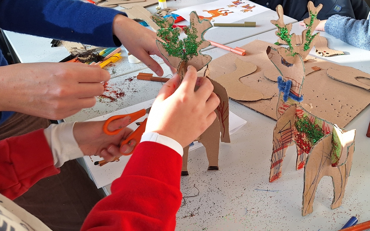Les mains des enfants fabriquent des rennes du père Noël avec des paillettes et des couleurs