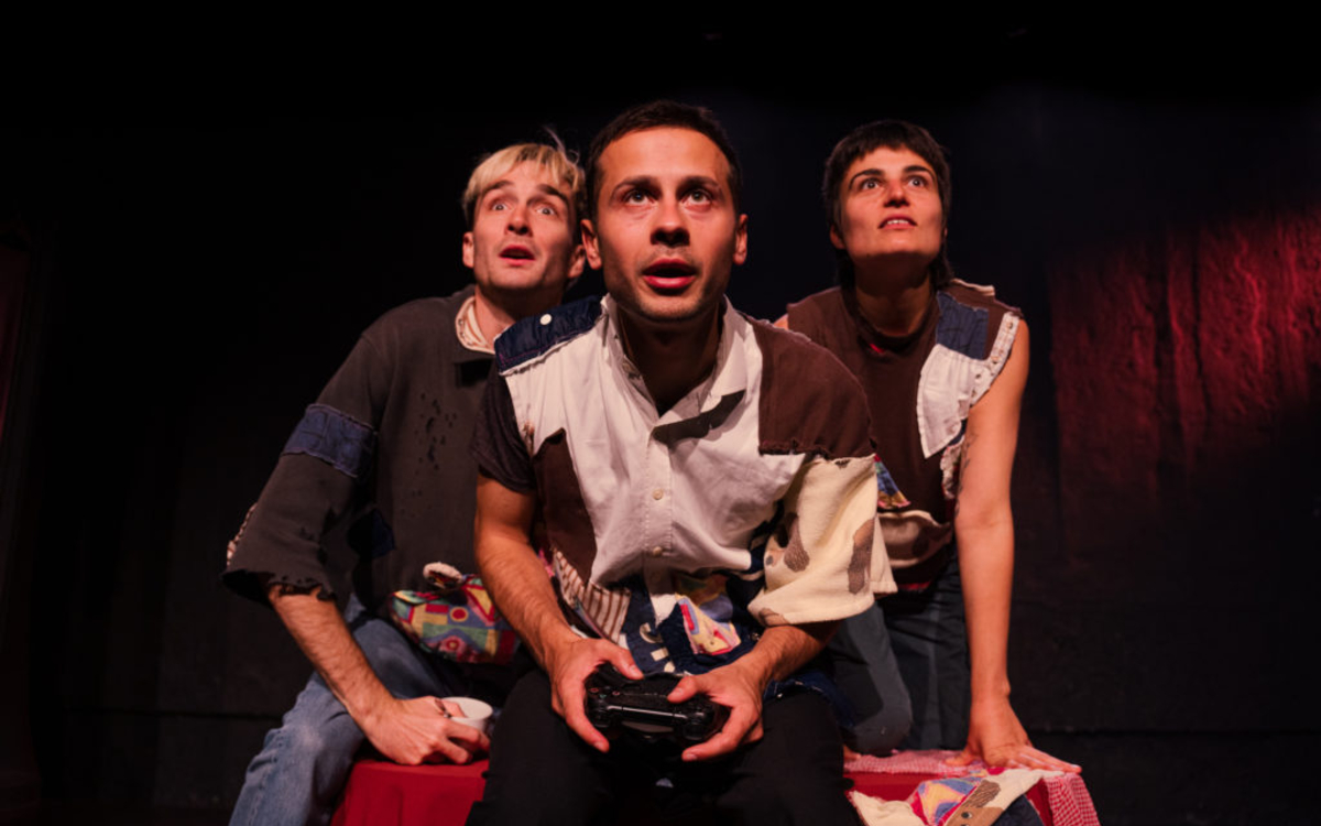 Sur une scène de théâtre, trois jeunes sont photographiés de près en train de jouer à la console