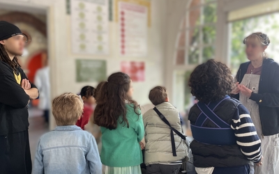 Des enfants écoutent une femme leur expliquer des choses, un accompagnateur est avec eux et écoute aussi