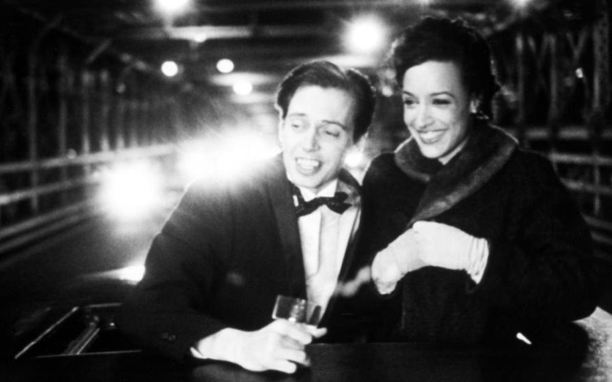 Steve Buscemi et Jennifer Beals dans In the Soup, vêtus de tenues de soirée, passent la tête hors d’une voiture décapotable.