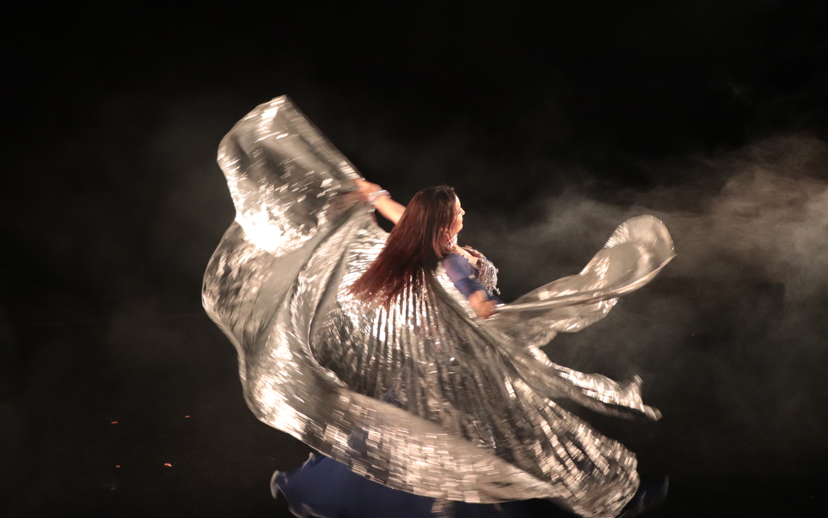 Une danseuse orientale danse sur scène avec un voile argenté