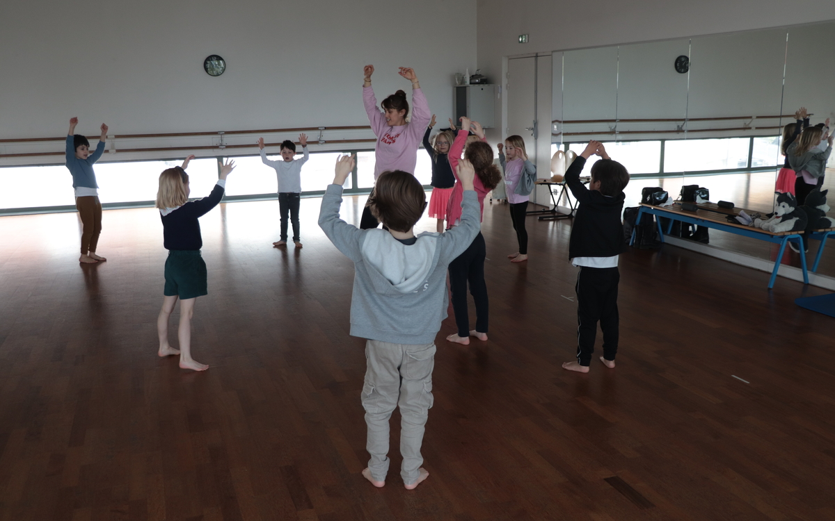 Des enfants entourent leur professeure et dansent en levant les bras