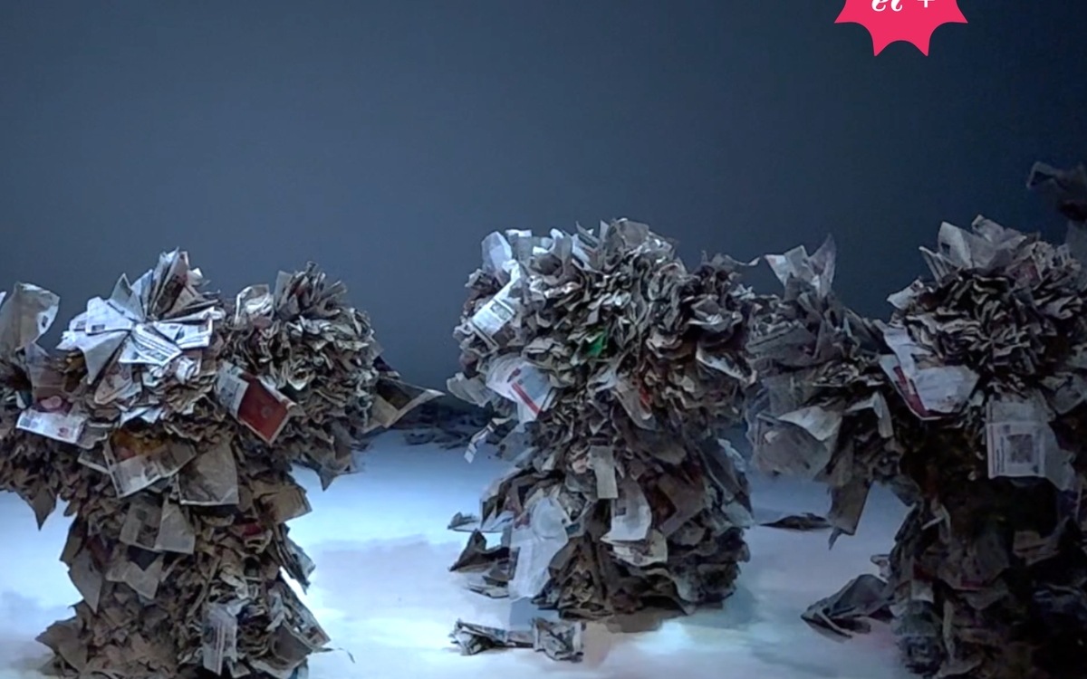 Trois grands personnages construites en papier journal sont sur la scène. 