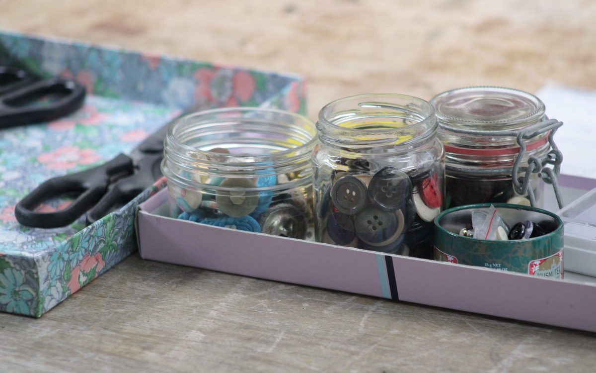 Photographie de boîtes contenant des boutons et des ciseaux, prise lors d’un atelier de couture à la main.