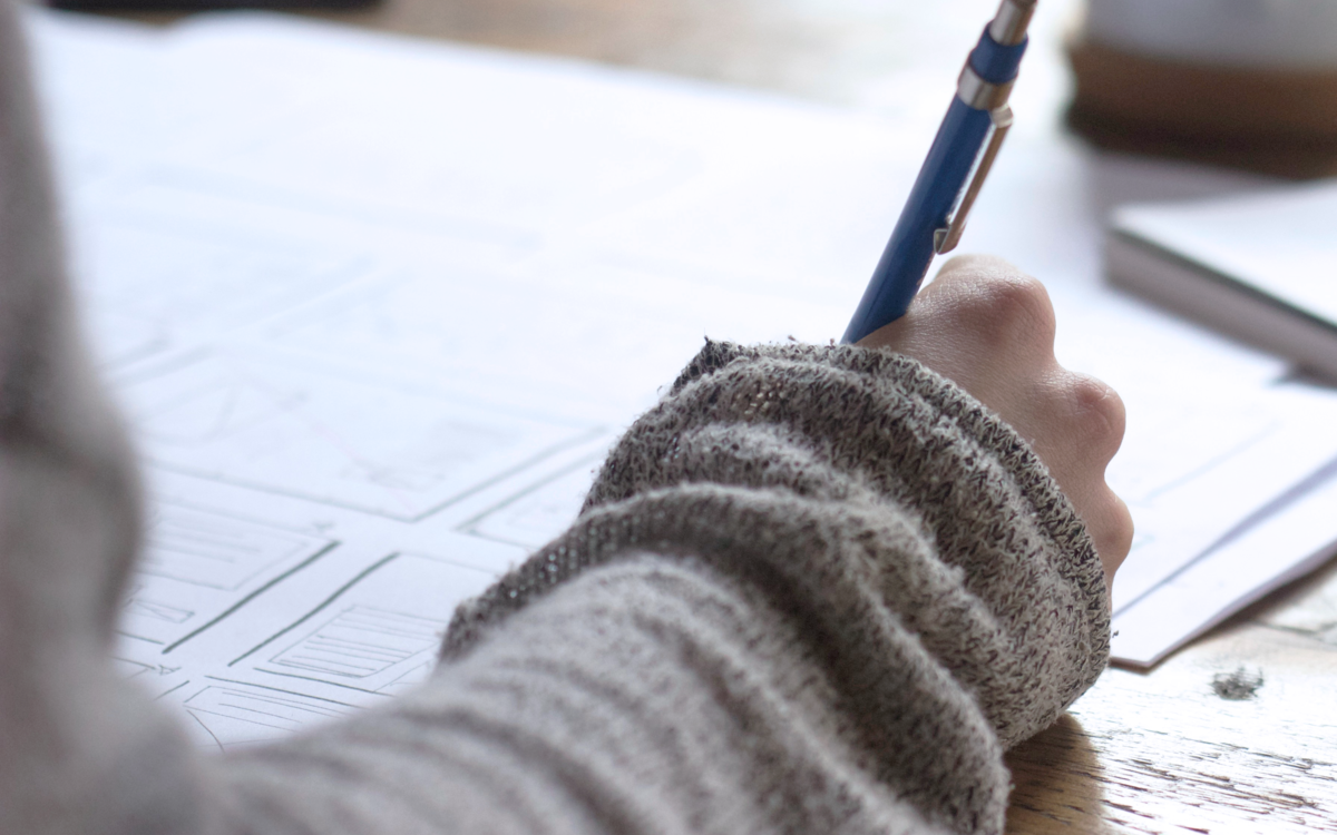 Photographie de la main d’une personne en train d’écrire un texte sur une feuille.