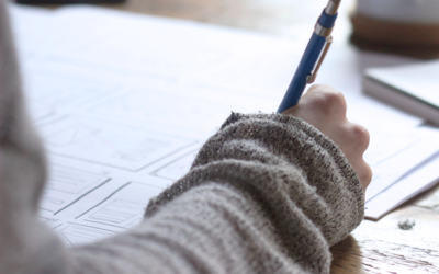 Photographie de la main d’une personne en train d’écrire un texte sur une feuille.