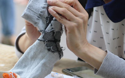 Photographie des mains d’une personne en train de raccommoder une chaussette.