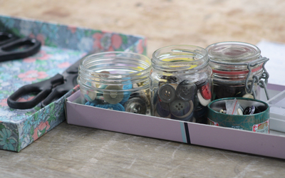 Photographie de boîtes contenant des boutons et des ciseaux, prise lors d’un atelier de couture à la main.