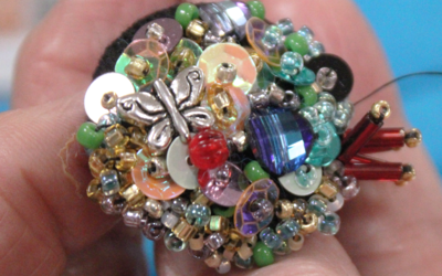 Photo d'une main tenant une broche sur laquelle ont été brodées des perles afin de la personnaliser. Création qui a été réalisée lors de l'atelier broderie de perles sur bouton. 