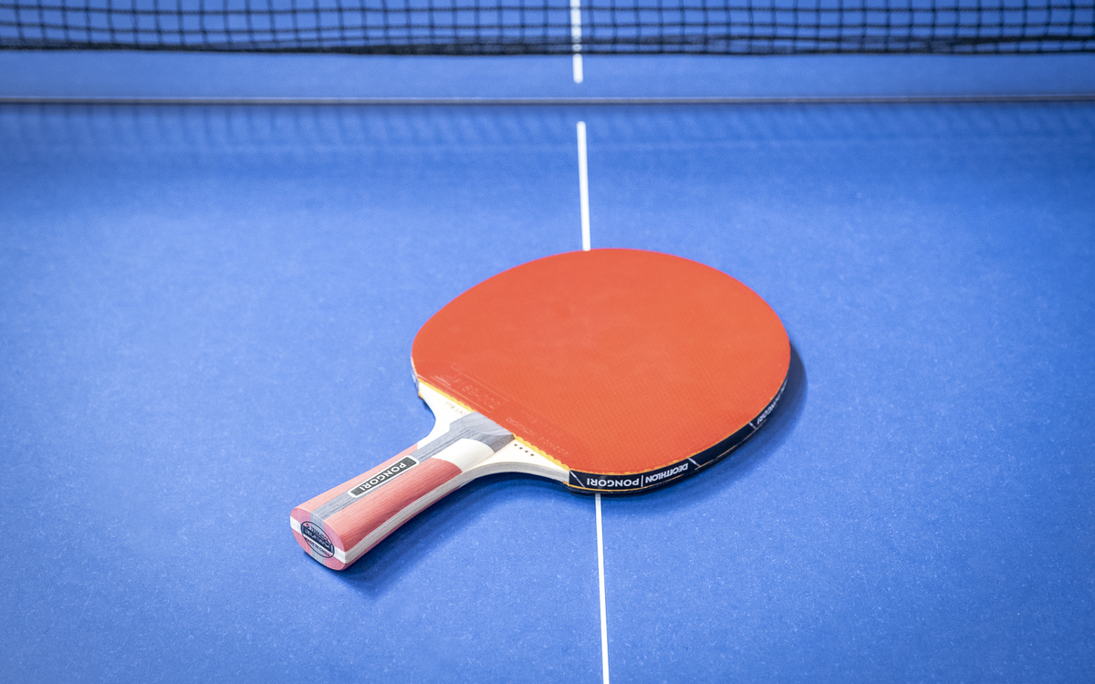 Photo d'une raquette de ping-pong rouge sur une table bleue.
