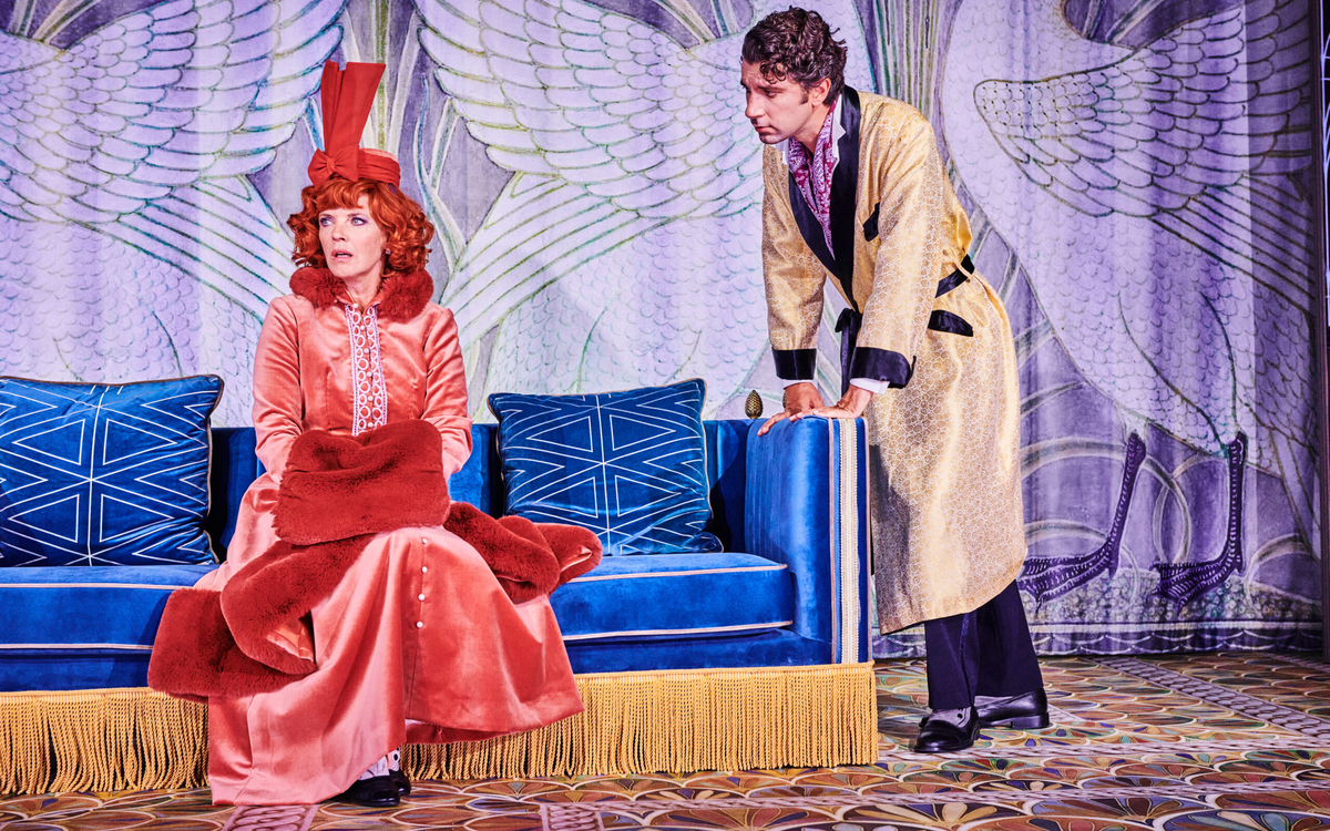 Sur une scène de théâtre, une femme assise sur un canapé et un homme debout