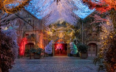 Cour pavée ornée de décors hivernaux et de branches lumineuses, devant une façade ancienne illuminée.