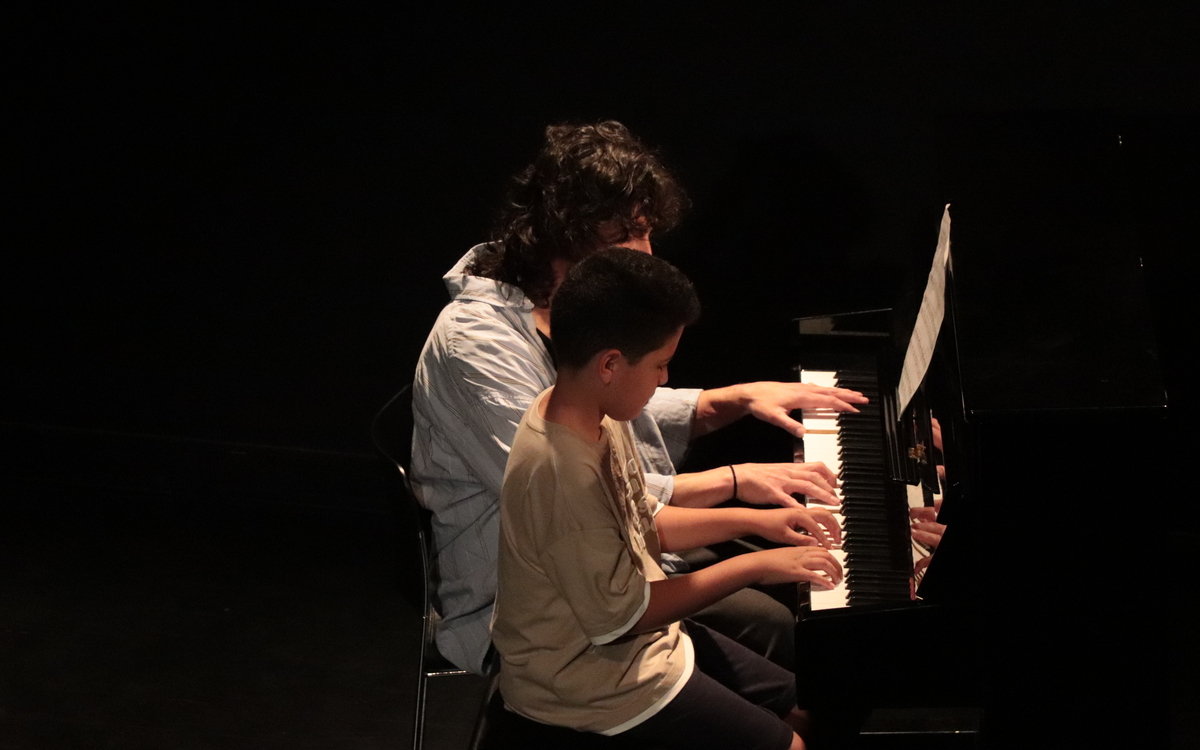 Un adulte et un enfant jouent au piano à 4 mains sur une scène
