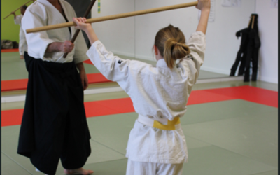 Une petite fille s'exerce à l'Aïkido avec un bâton contre un professeur avec un bâton