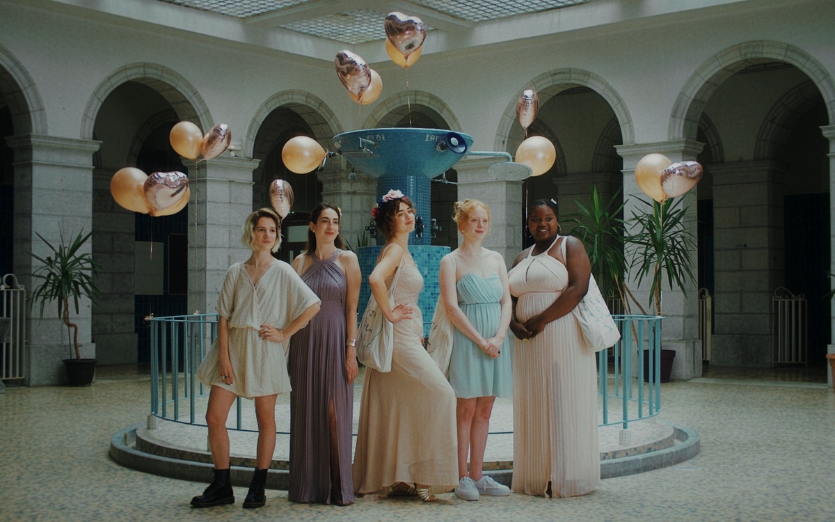 Cinq jeunes femmes élégamment vêtues posent côte à côte dans un bâtiment thermal. 