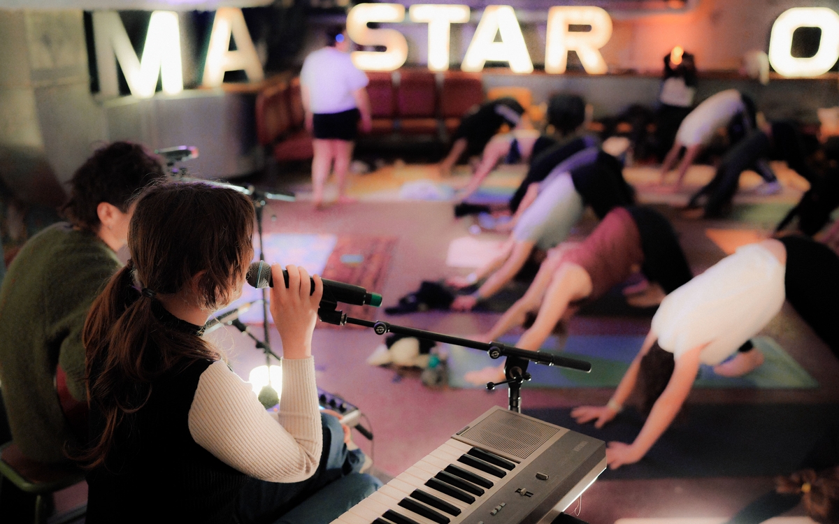 L'artiste Estelle Mortelle et le musicien Adrien au premier plan, chantent et jouent devant un public de yogis.