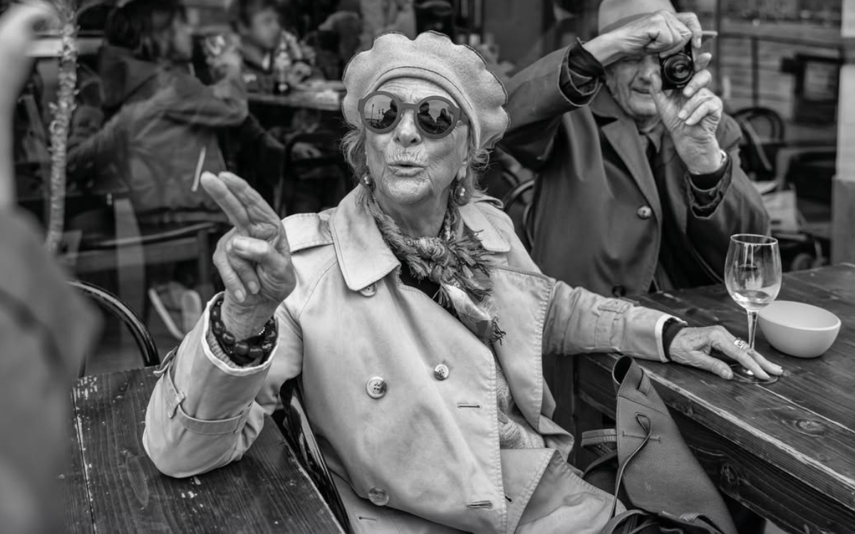 Photographie en noir et blanc représentant une femme âgée à une terrasse de café