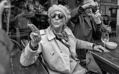 Photographie en noir et blanc représentant une femme âgée à une terrasse de café