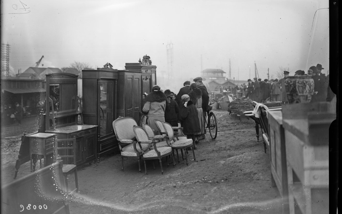 Photo d'époque en noir et blanc, personnes devant des armoires et fauteuils en plein air