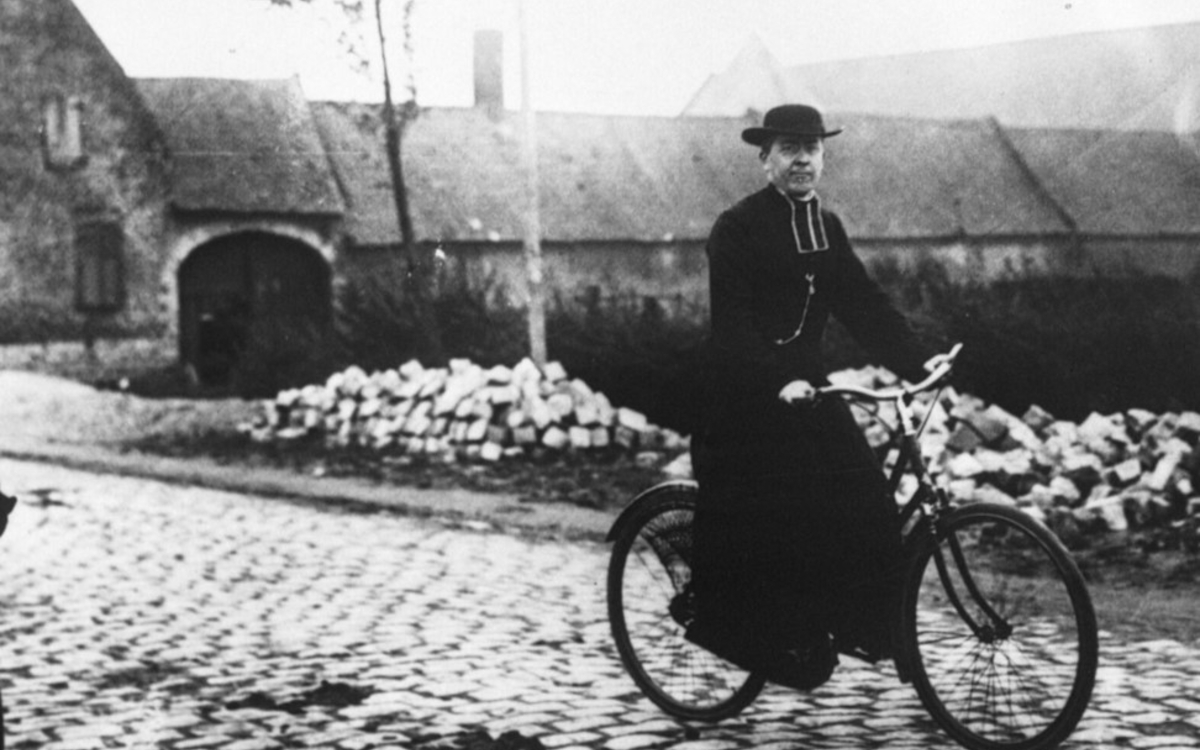 Photographie en noir et blanc montrant un prêtre en soutane pédalant à bicyclette