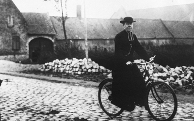 Photographie en noir et blanc montrant un prêtre en soutane pédalant à bicyclette