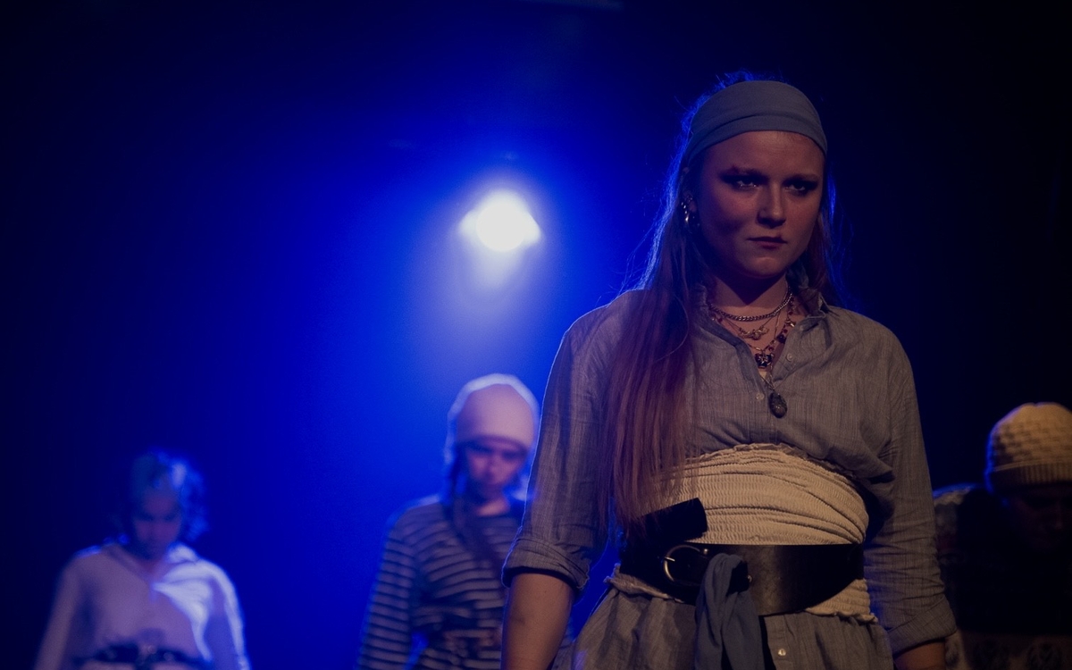 Des personnes jouent une scène du spectacle dans une lumière bleutée