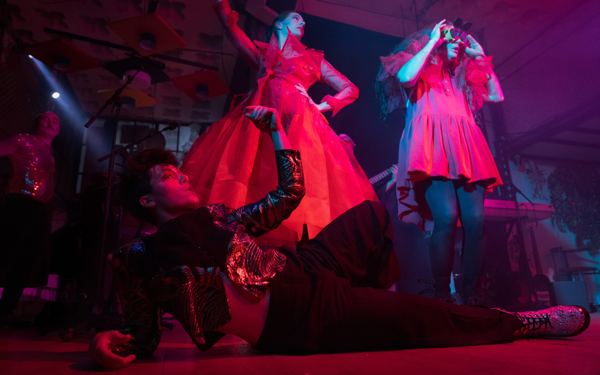 Scène de cabaret contemporain avec trois artistes aux postures et expressions burlesques, dans une ambiance théâtrale, dynamique et immersive.