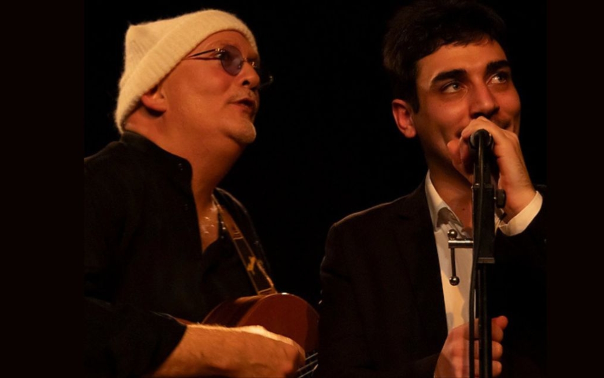 Achille V chante au micro aux côtés d’Hervé Delaiti à la guitare, sur scène, dans le spectacle musical Écoute-moi.