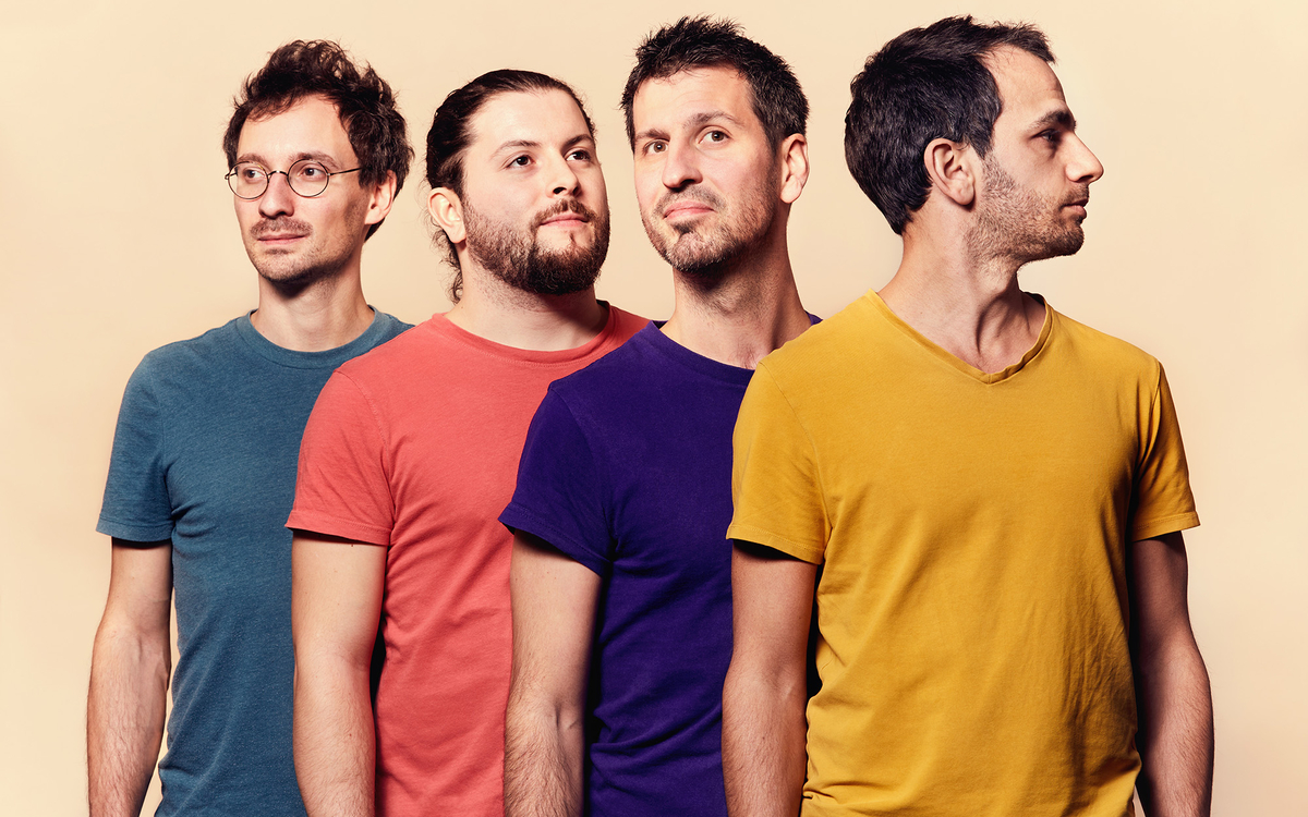 Quatre musiciens du groupe de pop française Bazar posent en portrait studio sur fond clair, alignés en diagonale et vêtus de t-shirts colorés, regardant vers la droite