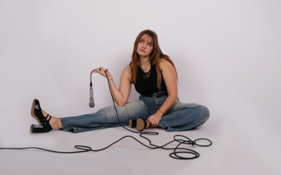 Chanteuse églantine assise par-terre avec un micro à la main, le regard évasif, sur fond blanc