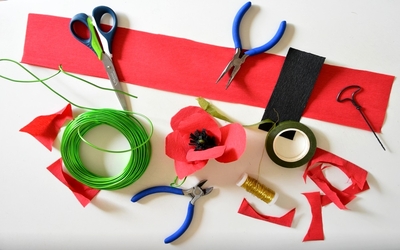 Matériel pour créer des coquelicots en papier: pince, ciseaux, fils de métal, papiers crépon rouge et noir, scotch de fleuriste vert