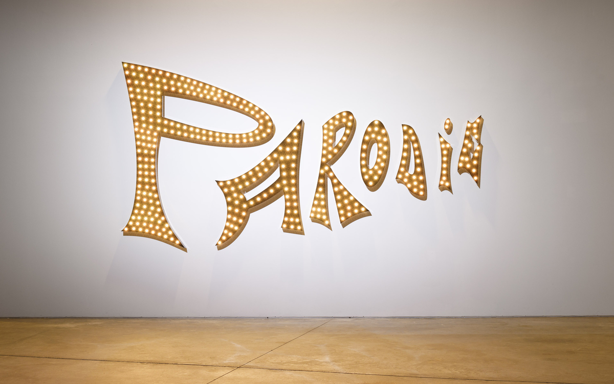 Une enseigne lumineuse avec des lettres esquissant le mot Parodie en une lumière dorée