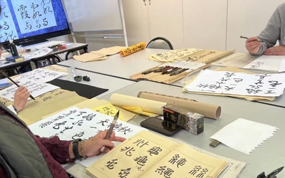 Atelier de calligraphie chinoise avec des participants écrivant au pinceau sur papier, encres et modèles de caractères sur table