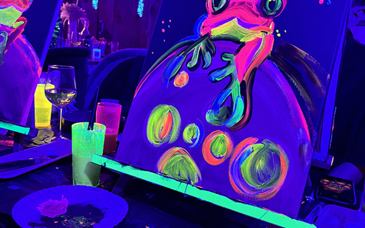 Toile de peinture fluorescente représentant une grenouille colorée, réalisée lors d’un atelier artistique sous lumière UV dans un espace immersif à Paris.