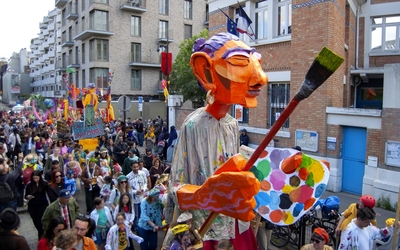Lors d'un carnaval, un Géant de couleur orange, habillé d'une chemise de peintre, tient un immense pinceau dans la main droite et une immense palette de couleur dans la main gauche. Il est au milieu d'une foule déguisée, suivi d'autres chars.