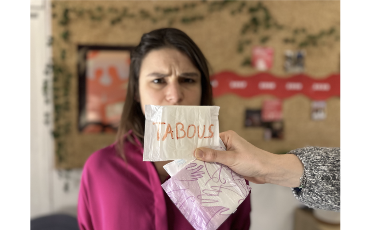 Une femme qui à la bouche couverte par une personne qui tend une serviette hygiénique avec écrit Tabou dessus. 
