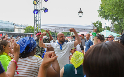 Johan Amselem guide un groupe de participant·es lors d’un bal participatif en plein air. Les personnes, de tous âges et horizons, dansent ensemble au Bassin de la Villette à Paris dans une ambiance festive et inclusive.
