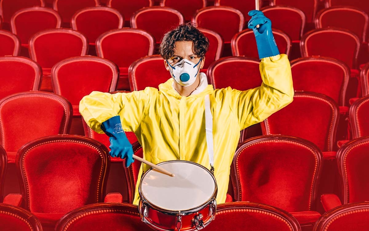 Homme assis dans les sièges d'un théâtre, portant un ciré jaune et faisant des percussions