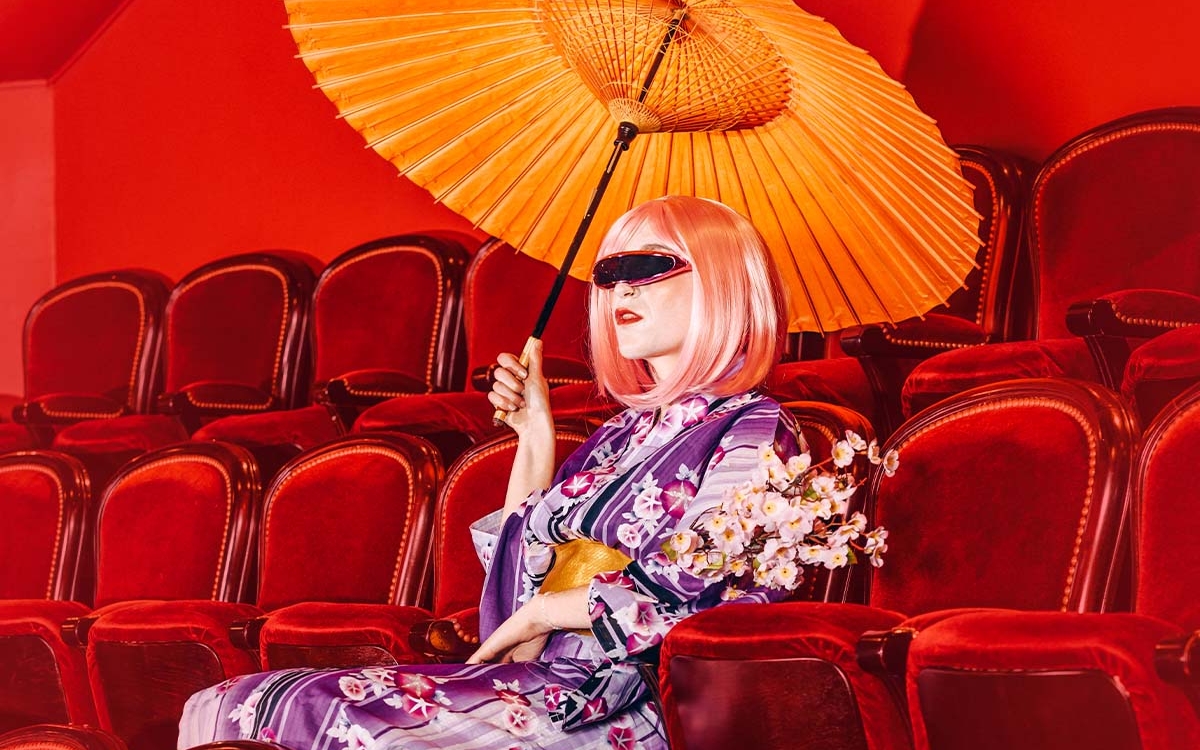 Femme assise dans les fauteuils d'un théâtre, habillée en Geisha avec des lunettes futuristes