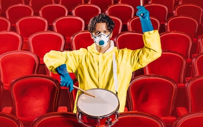 Homme assis dans les sièges d'un théâtre, portant un ciré jaune et faisant des percussions