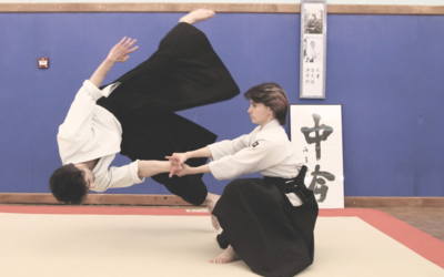 Deux personnes en tenue d'aikido. Une femme projette un homme.