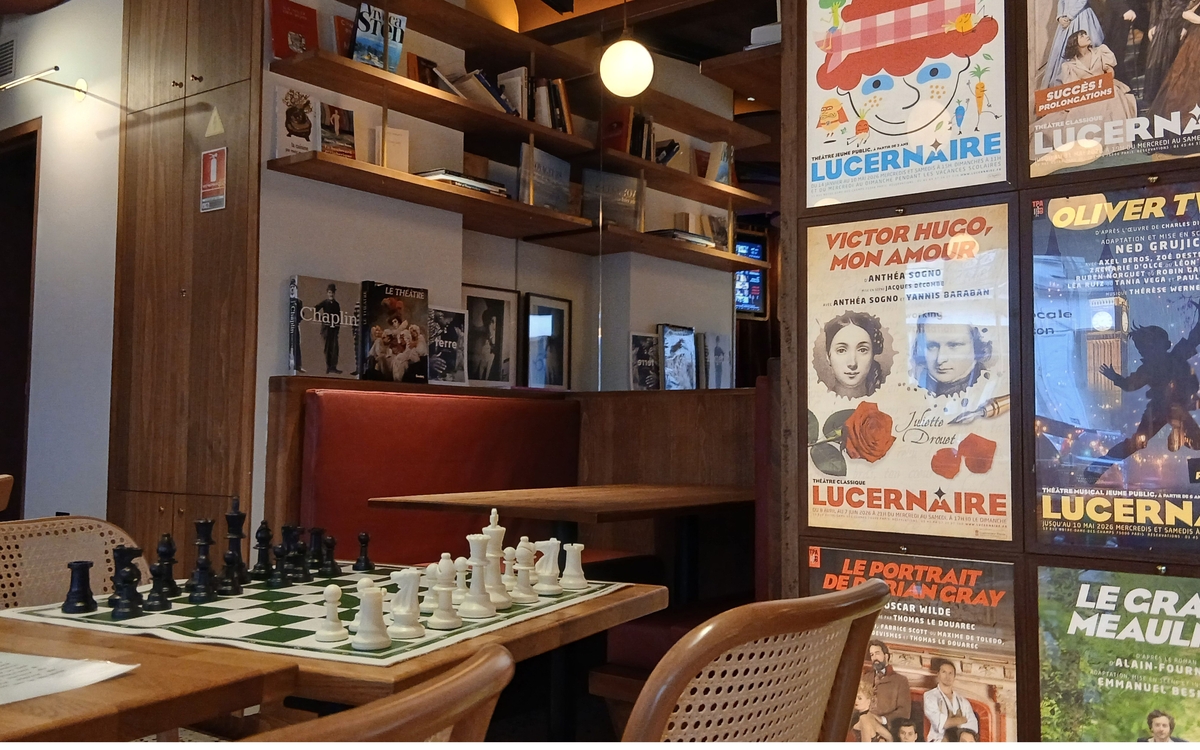 Echiquier posé sur une table avec affiches de pièces de théâtre dans le fond. La photo montre l’ambiance du kawaa du Lucernaire, qui est un théâtre à Paris.