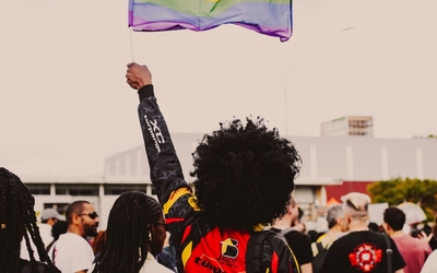 Photo d'une femme prise de dos brandissant le drapeau LGBTQIA+