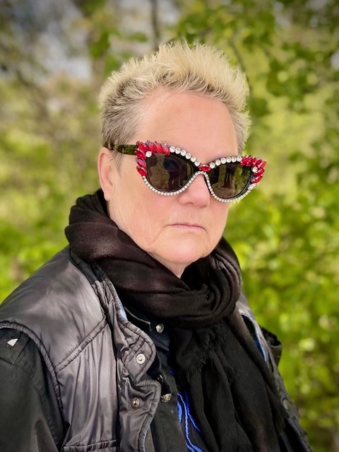 Portrait de Beth Stephens avec des cheveux courts et des lunettes de soleil à strass rouges et blancs