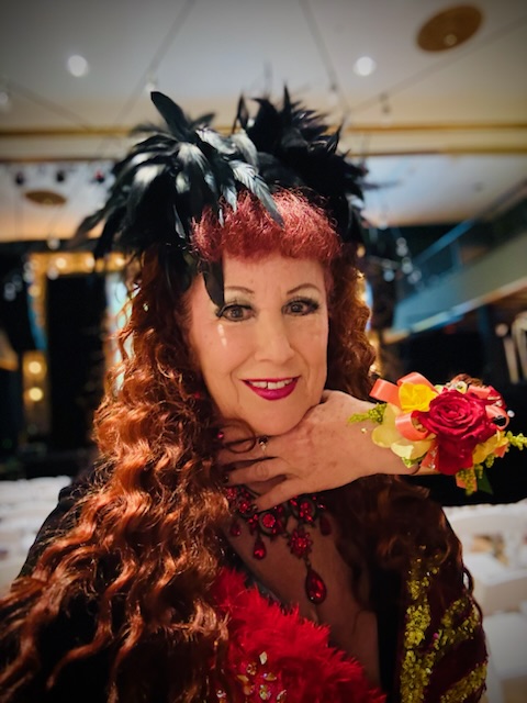 Portrait d'Annie Sprinkle maquillée et habillée en costume à plumes avec des cheveux rouges