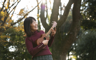 Une femme souriante joue du Ukulele debout dans un parc 