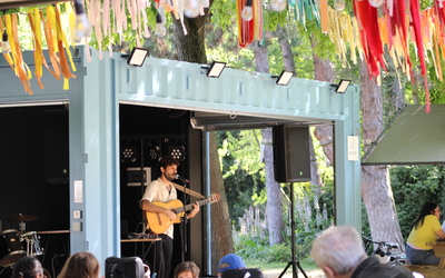 Photographie d'un guitariste en concert live sur la scène haute en couleurs de la Guinguette Créative